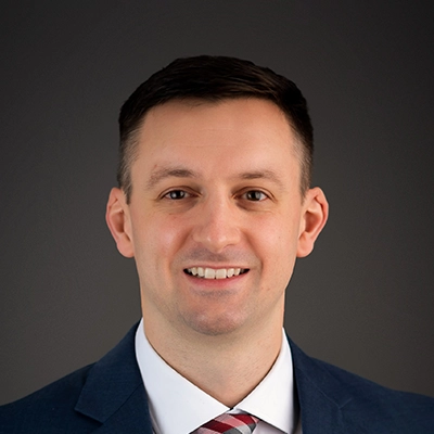 Chiropractor Jason Ballweg Smiling In Front Of Grey Background