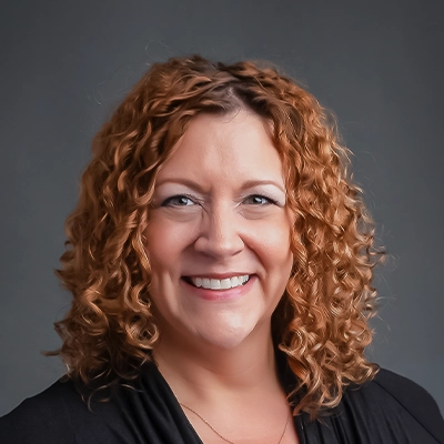 Chiropractor Sara Kirkman Smiling In Front Of Grey Background